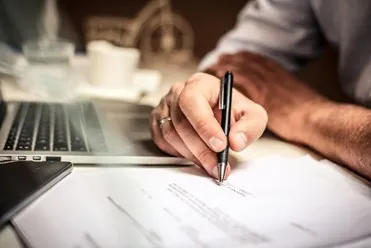 Person signing a document at a desk with a laptop